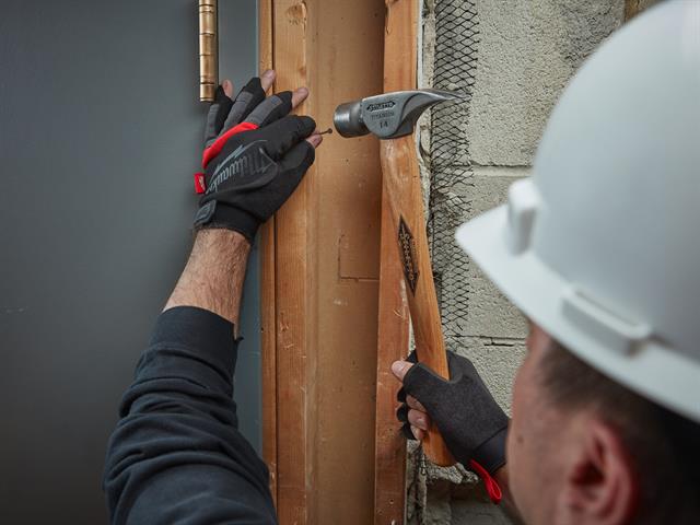 A construction working hammering in a nail with fingerless gloves on