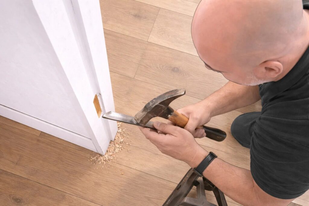 How to Hang an Internal Door: Step by Step Guide for a Perfect Fit 8 Illustration of a person using a hammer and chisel to cut a recess into a door frame, with wood chippings on the floor below.