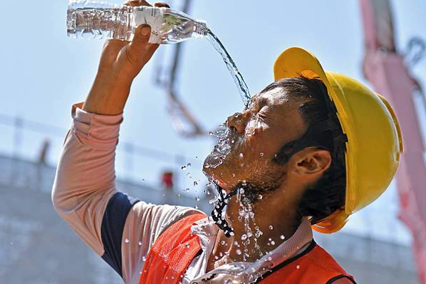 How to Stay Cool on Site During a UK Heatwave 1 Construction worker wearing a hard hat and high visibility vest pouring water over his face on a building site to cool down, demonstrating a practical way to manage heat exposure and stay safe while working in hot weather conditions.