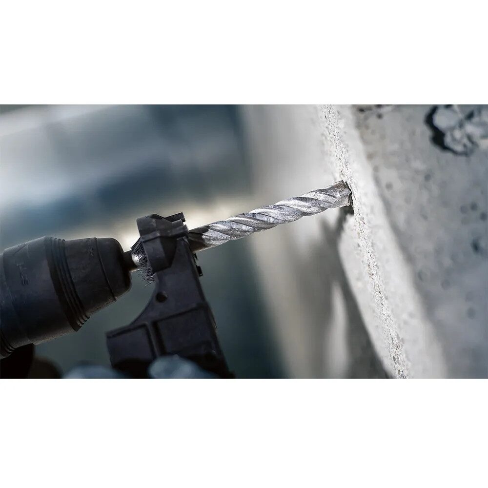 Drill Bits Buying Guide: Choosing the Right Drill Bit for Every Material 4 Action shot of an SDS masonry drill bit fitted to a rotary hammer drill as it drills into a concrete wall. The spiral flutes of the bit are visible as the carbide tipped head penetrates the masonry surface. A depth stop attachment is mounted alongside the drill bit to help achieve a consistent drilling depth. The background is blurred, focusing attention on the drilling process and the concrete substrate.
