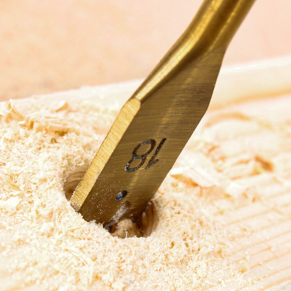 Drill Bits Buying Guide: Choosing the Right Drill Bit for Every Material 16 Extreme close up of a spade drill bit boring into a piece of timber. The flat paddle shaped bit, marked with the size "18", is cutting a large diameter hole while producing fine wood shavings and sawdust around the drilling area. The image highlights the broad cutting edges and centre point design of a spade bit, commonly used for fast drilling of larger holes in wood.