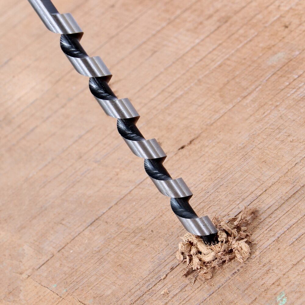 Drill Bits Buying Guide: Choosing the Right Drill Bit for Every Material 17 Close up image of an auger drill bit boring into a wooden surface. The bit features a deep spiral flute design that efficiently removes wood chips and shavings as it cuts. Fresh wood debris is visible around the entry point, demonstrating the auger bit's ability to drill deep, clean holes in timber while clearing waste material from the hole during drilling.