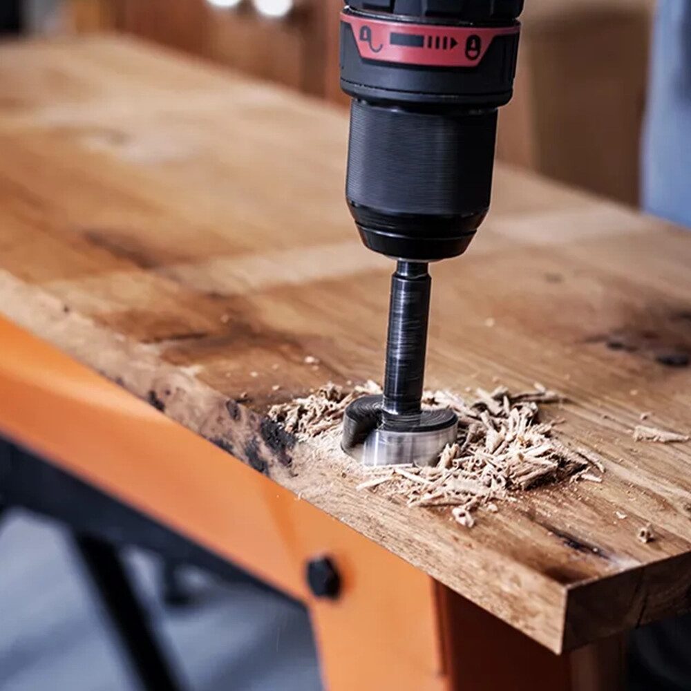 Drill Bits Buying Guide: Choosing the Right Drill Bit for Every Material 22 A close up of a cordless drill fitted with a Forstner drill bit boring a clean flat bottomed hole into a wooden workbench. Fresh wood shavings surround the hole as the bit cuts into the timber, with the drill positioned vertically above the work surface. The blurred workshop background and sturdy bench create a practical woodworking setting, highlighting precision drilling and joinery applications.