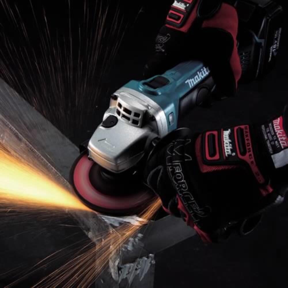 Close up of a Makita cordless angle grinder cutting through metal, producing bright orange sparks while being operated with gloved hands against a dark background.