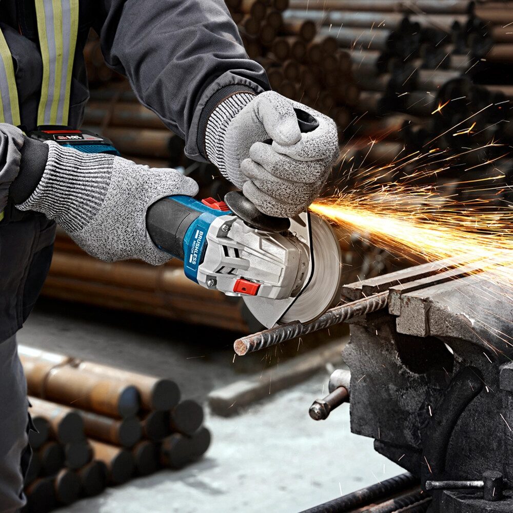 Close up of a cordless angle grinder cutting through steel rebar secured in a bench vice, with bright sparks flying as the operator wears protective gloves and controls the tool with both hands in a workshop.